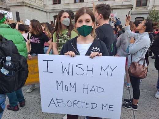 An abortion protestor holding a sign saying she wished her mother had aborted her.