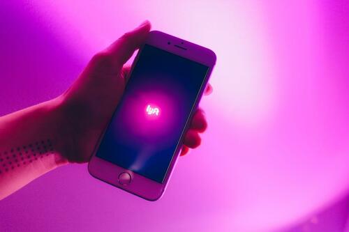 A hand holding a smartphone showing the Lyft app.