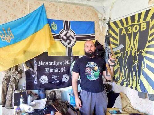 A man poses in front of flags representing Ukrainian Neo-Nazi groups, including the aptly-named Misanthropic Division.