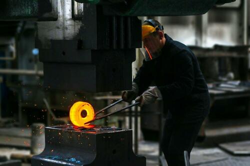A worker holding a hot steel ring with tongs.