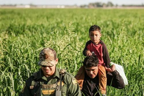 A Border Patrol agent leads illegal immigrants through farmland after they were captured by agents near the U.S.–Mexico border barrier in Yuma, Ariz., on May 21, 2022. (Mario Tama/Getty Images)