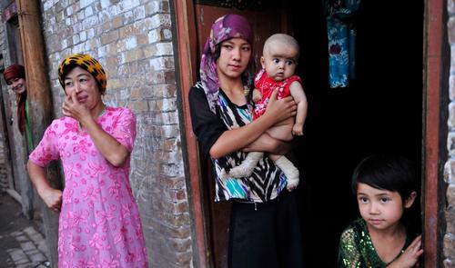 An ethnic Uighur woman hugs her son as she stands outside her house with her daughter and neighbors at an old residential area of Kashgar, Xinjiang Uighur Autonomous Region, July 22, 2012.